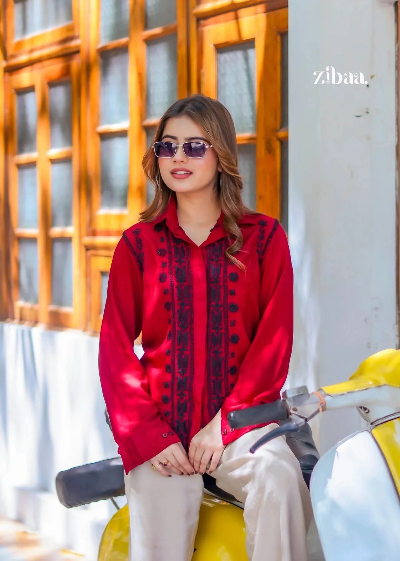 The model poses relaxed and casual while seated on the scooter, highlighting the fine black threadwork on her red chikankari shirt.