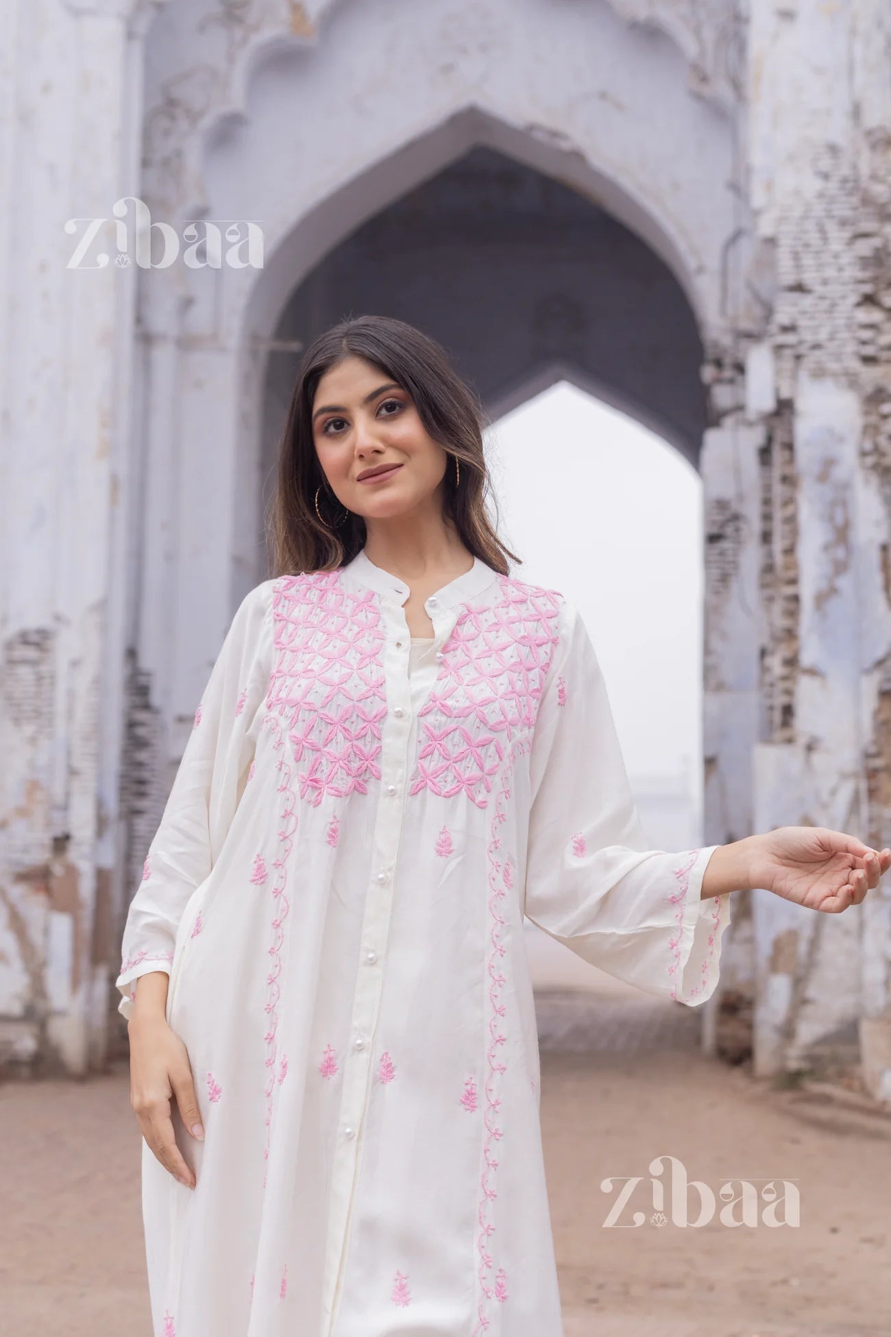 Woman wearing a white chikankari kurta with pink geometric embroidery, standing outdoors in natural light.