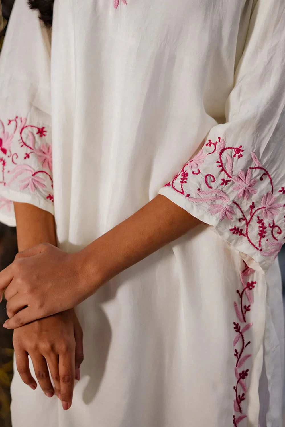 Close-up view of pink chikankari embroidery on cuffs and other sections of a white chikankari kurti.