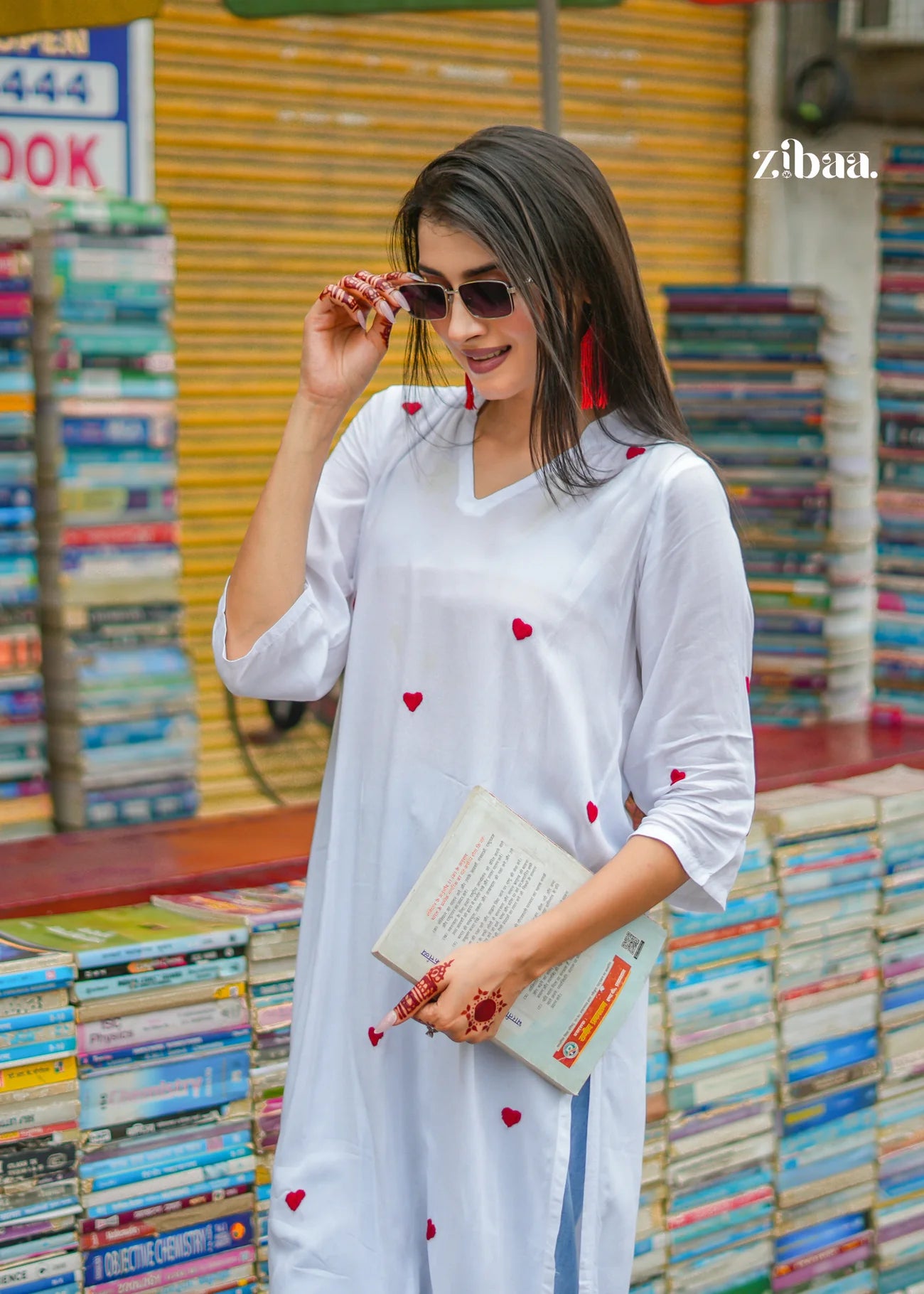 The model poses casually just outside a book stall, wearing a white chikankari kurti with delicate red heart motifs, blending effortlessly into the everyday street scene.