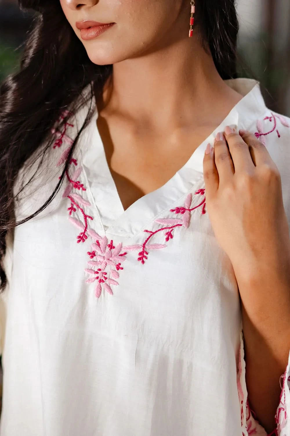Close-up view of pink embroidery on V-pattern neckline of a white chikankari kurti.