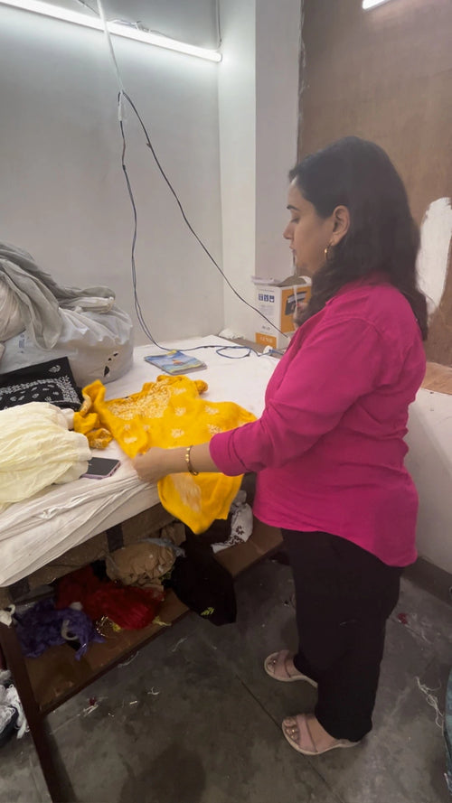 Woman in pink shirt working on a table and examining the quality of yellow Chikankari garment