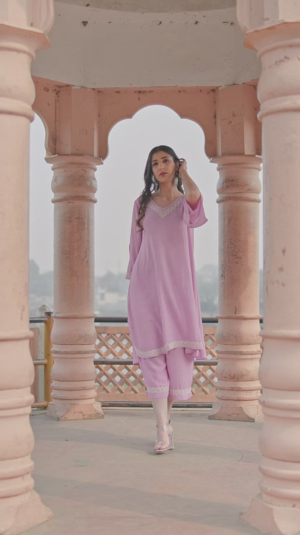 Girl in a pastel pink Chikankari Kurta Set with delicate embroidery on the neckline, gently touching it while posing outdoors gracefully