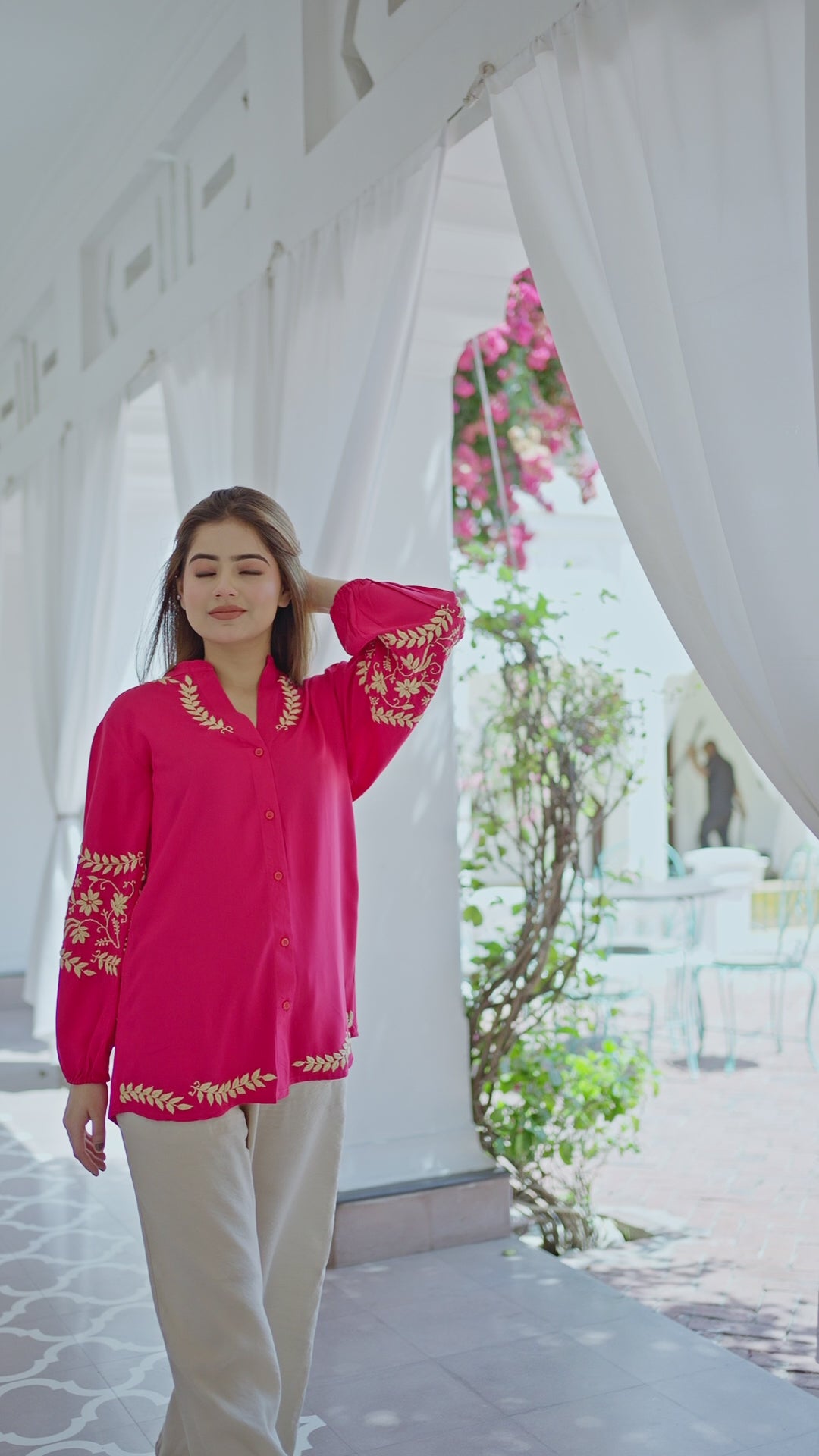 The model is showcasing a Hot Pink Kurta with Golden Embroidery while walking in an airy corridor. Hot Pink Kurta with Golden Embroidery pairs beautifully with neutral trousers. The graceful stance enhances the festive and casual appeal.