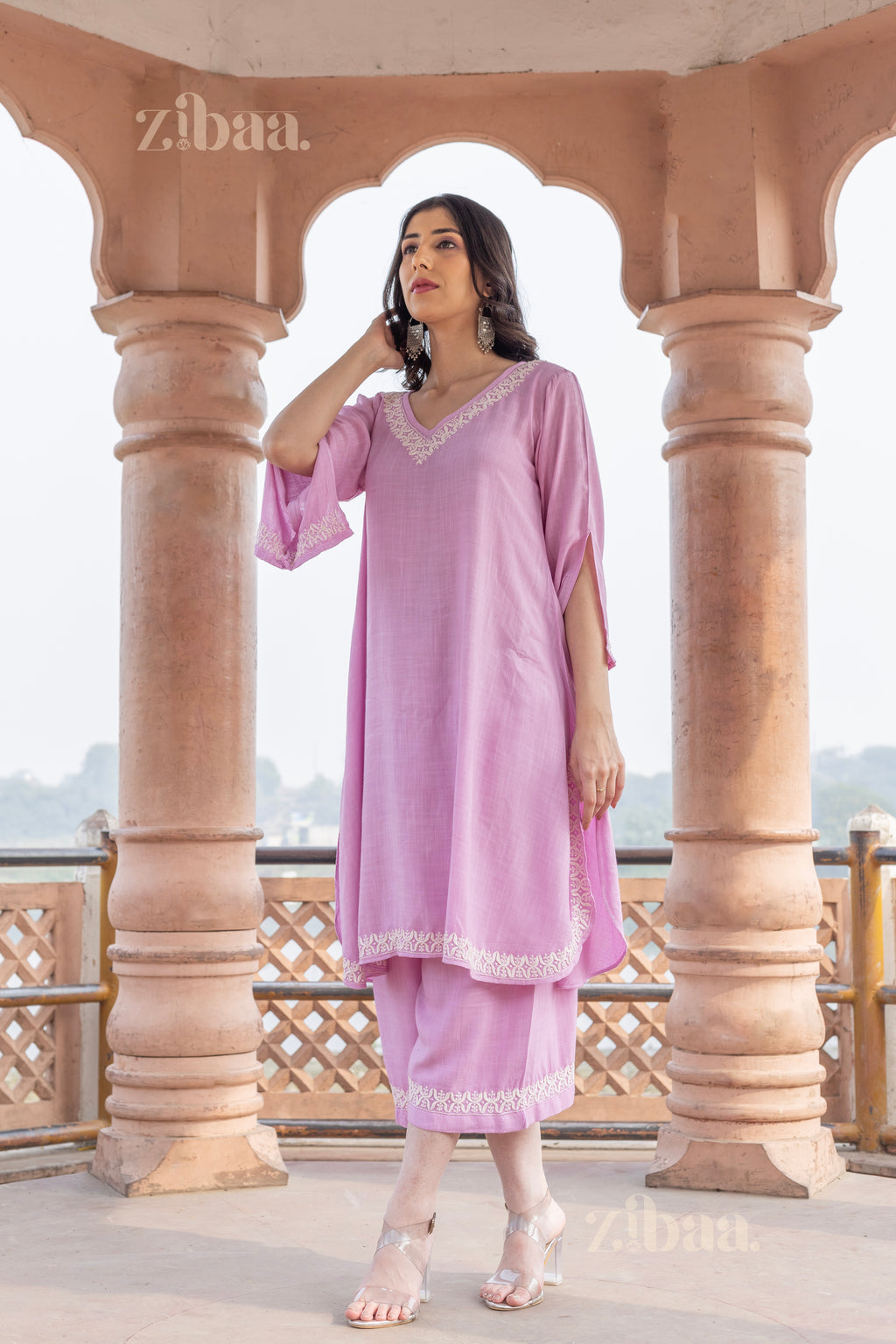 Girl in a pastel pink Chikankari Kurta Set with delicate embroidery on the neckline, gently touching it while posing outdoors gracefully