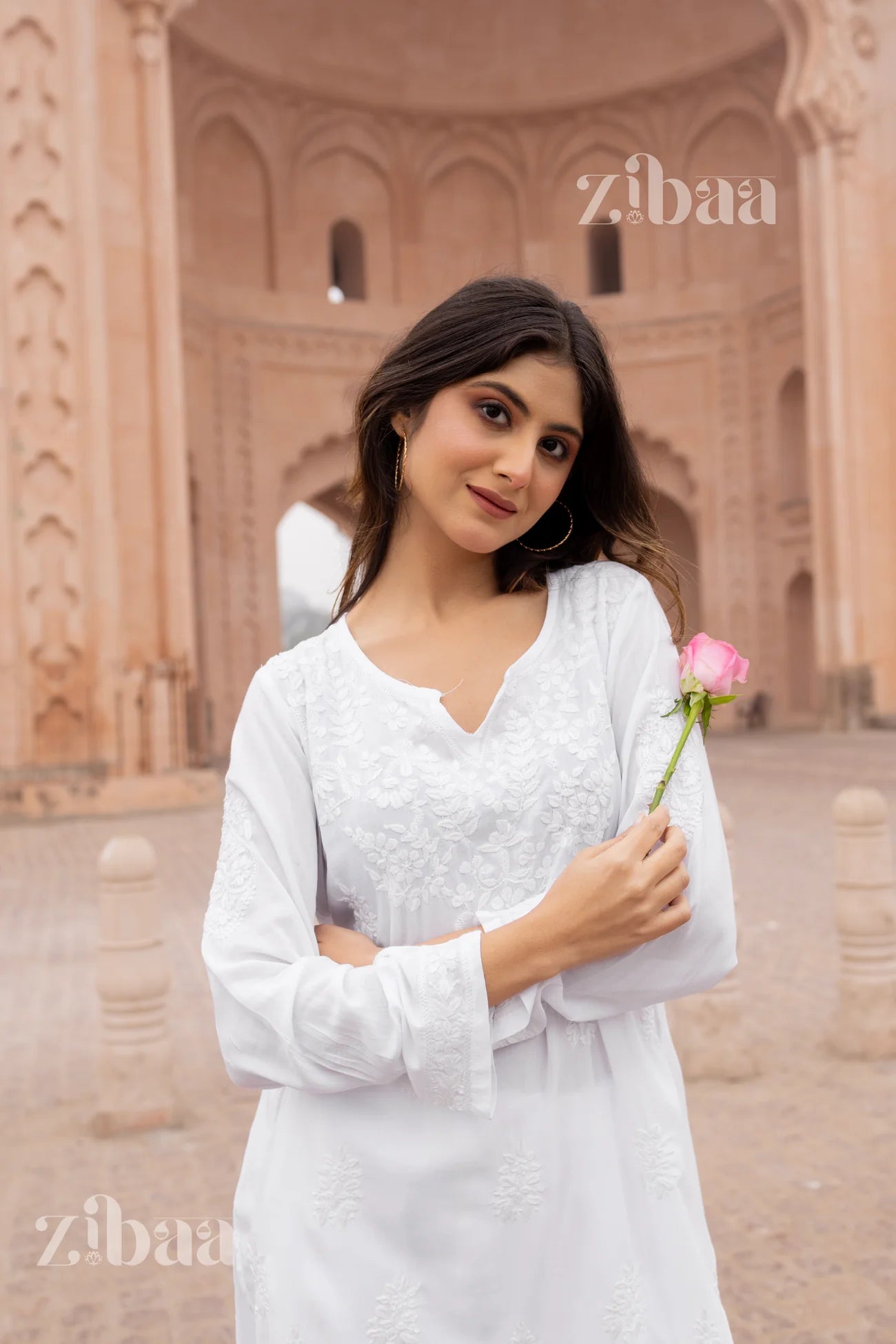 Woman in a white embroidered dress holding a pink rose, with 'zibaa' branding.
