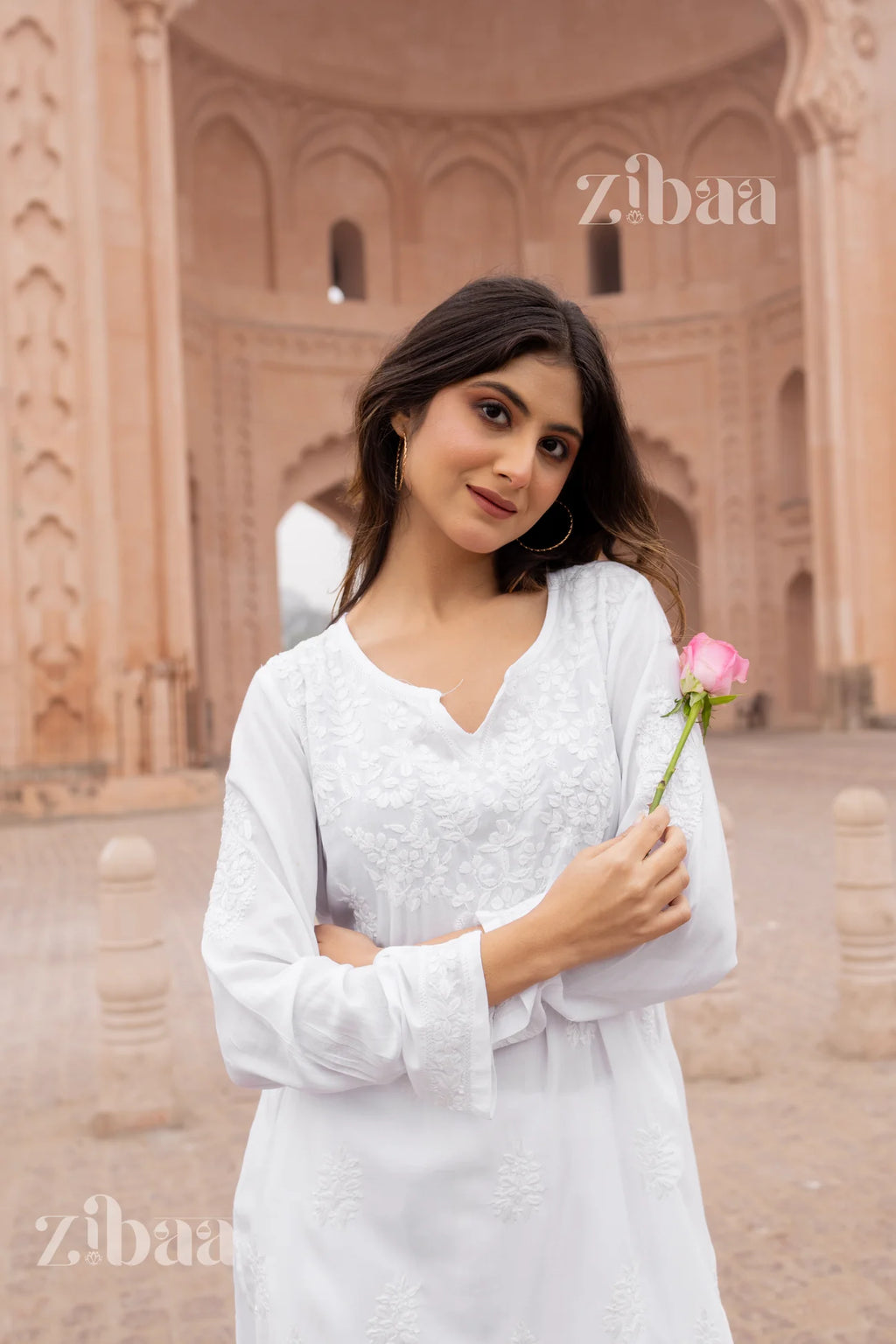 Woman in a white embroidered dress holding a pink rose, with 'zibaa' branding.