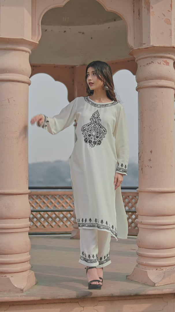 A woman wearing a white Chikankari Anarkali with intricate embroidery poses elegantly outside a heritage building in natural light