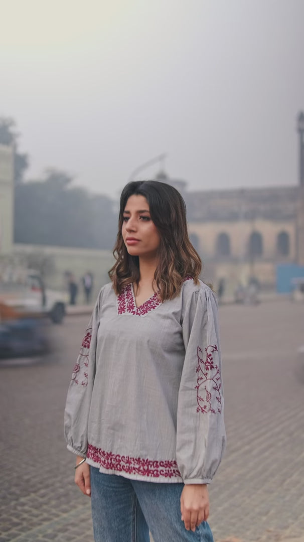 Partial view of a woman wearing a grey Chikankari top with red embroidery on the neckline and sleeves, paired with statement earrings