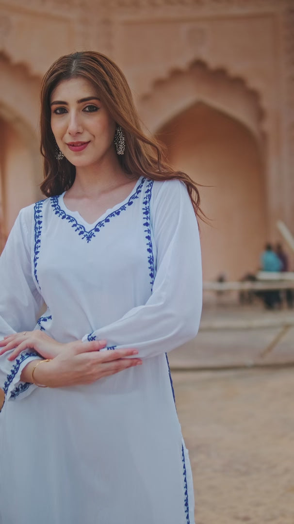 Close-up of a woman showcasing a white kurti for women with intricate blue floral embroidery, pointing to the detailed side design